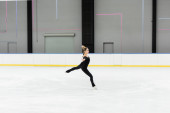 full length of professional figure skater in bodysuit skating with outstretched hands in ice arena 