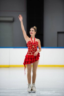 Kırmızı elbiseli mutlu artistik patinajcı ve buz arenasında el sallayan altın madalya sahibi.