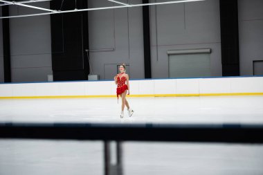 Kırmızı elbiseli güler yüzlü patenci elinde altın madalya ve buz arenasında paten tutuyor.