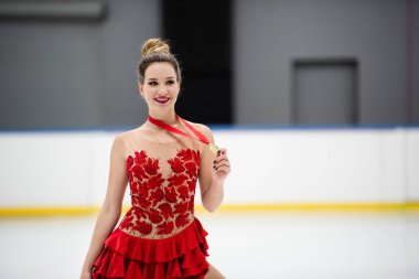 Kırmızı elbiseli mutlu artistik patinajcı elinde altın madalyayla 