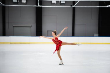 Kırmızı elbiseli artistik patinajcı profesyonel buz arenasında deve dönüşü yapıyor.