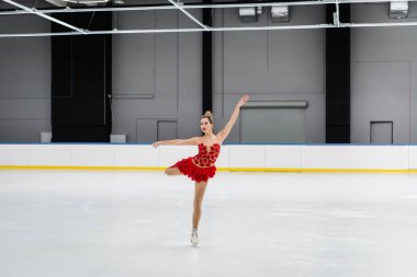 Kırmızı elbiseli artistik patinajcı buz arenasında deve dönüşü yapıyor.