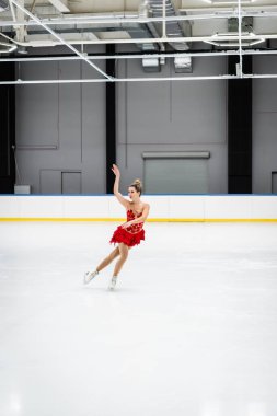 Profesyonel buz arenasında artistik patinaj ve jest yapan tam boy genç kadın.