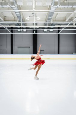 Profesyonel buz arenasında artistik patinaj yaparken bükülen genç bir kadın.