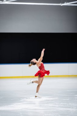 full length of happy figure skater with raised hands doing layback in professional ice arena clipart