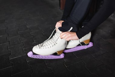 Genç bir kadın bankta otururken artistik patinaj ayakkabıları bağlıyor. 
