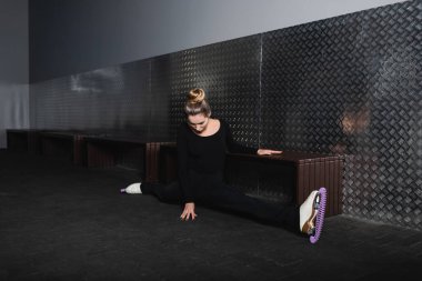 Beyaz artistik patenli genç bir kadın duvarın yanında iki büklüm oluyor.