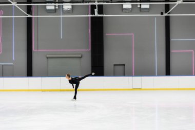 Profesyonel buz arenasında paten kayan siyah elbiseli genç bir kadının yan görüntüsü