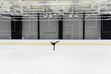 Profesyonel buz arenasında buz pateni yapan siyah elbiseli artistik patinajcının yan görüntüsü