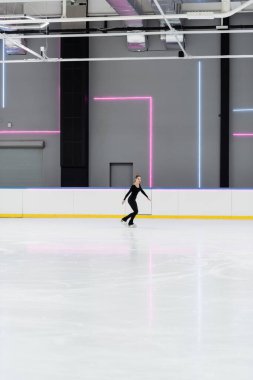 Profesyonel buz arenasında buz pateni yapan siyah elbiseli artistik patinajcı.
