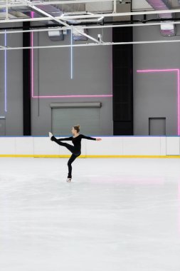 Profesyonel buz arenasında antrenman yapan siyah elbiseli artistik patinajcı.