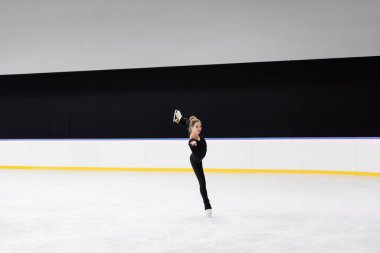 Donmuş buz arenasında buz pateni yapan siyah elbiseli artistik patinajcı.