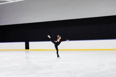 Siyah elbiseli artistik patinajcının yan görüntüsü profesyonel buz arenasında uzanmış elle kayıyor.