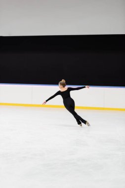 Buz arenasında uzanmış elleri olan, siyah elbiseli profesyonel artistik patinajcı.