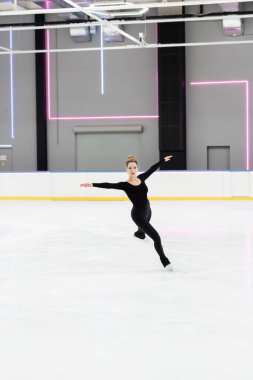 Profesyonel artistik patinajcıyla buz arenasında, neon ışıklarıyla uzanan siyah elbiseli patenci.