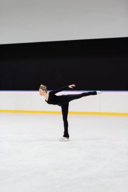Donmuş buz arenasında uzanmış siyah elbiseli profesyonel artistik patinajcı.