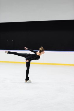 Profesyonel artistik patinajcının buz pateni pistinde uzanan elleri ile kayarken yan görüntüsü