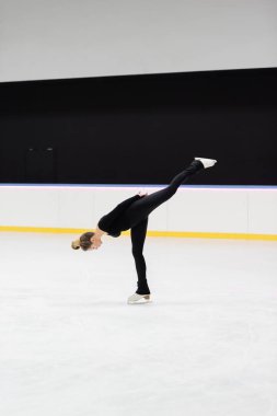 Buz arenasında buz bükerken siyah elbiseli profesyonel artistik patinajcı