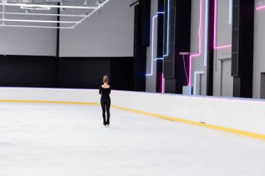 Donmuş buz arenasında siyah mayo ve buz pateni giymiş genç artistik patinajcının arka görüntüsü