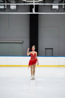 Kırmızı elbiseli neşeli artistik patinajcı buz pistinde altın madalya gösteriyor.