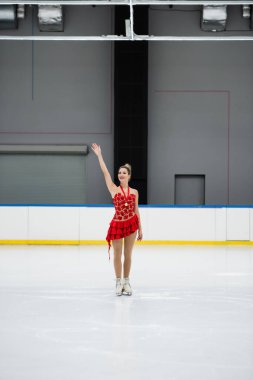 Kırmızı elbiseli neşeli artistik patinajcı elinde altın madalya ve buz arenasında el sallıyor.