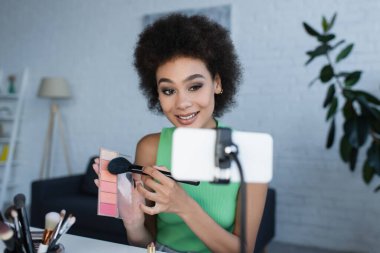Evde bulanık akıllı telefonun yanında yüzü kızaran Afrikalı Amerikalı blogcu 