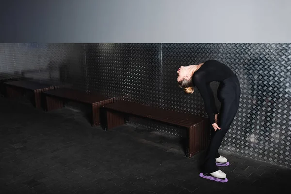 Beyaz figür paten giyen genç bir kadın duvara yaslanırken geriliyor.