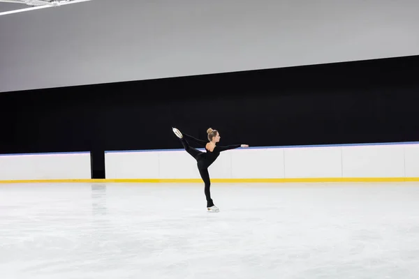 专业冰场用伸出手的黑色泳衣花样滑冰运动员侧视图 — 图库照片