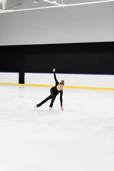 全长的年轻花样滑冰选手 身穿黑色运动服 手伸展开 在竞技场触摸冰冷的冰块 — 图库照片