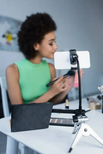 stock image Cellphone and decorative cosmetics near blurred african american woman at home 