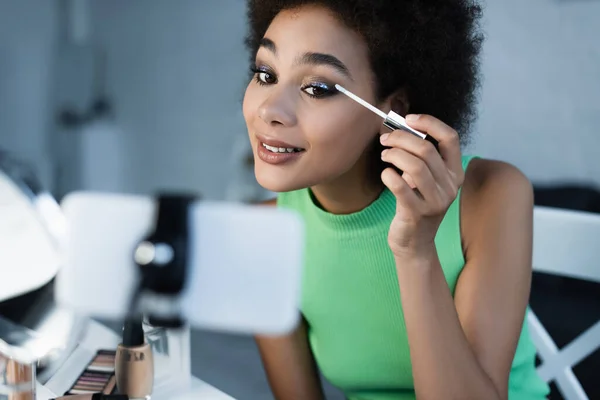 Blogger Afroamericano Positivo Mirando Teléfono Inteligente Mientras Aplica Sombras Ojos — Foto de Stock