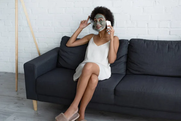 笑顔アフリカ系アメリカ人女性とともに粘土マスク顔上のスマートフォン上で話す上でソファに家 — ストック写真