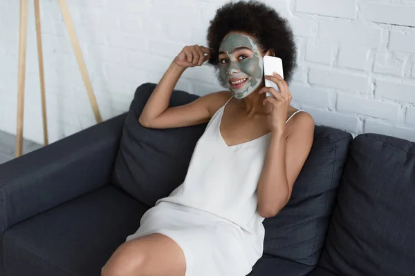 笑顔アフリカ系アメリカ人女性とともに粘土マスク顔上のスマートフォン上で話す上のソファ — ストック写真