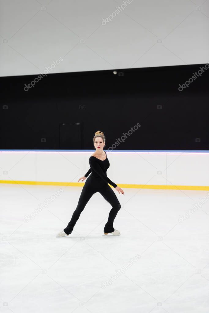 full length of professional figure skater in bodysuit skating in ice arena