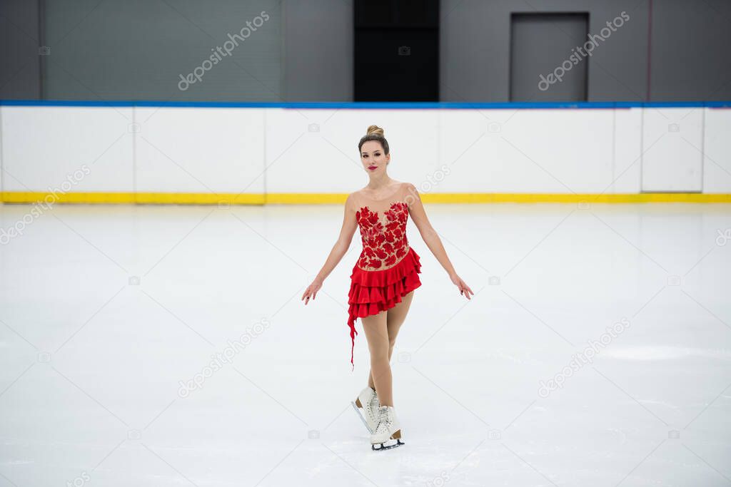 full length of young woman in red dress figure skating in professional ice rink