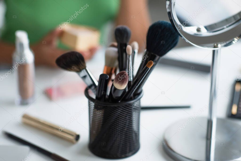 Cropped view of cosmetic brushes near mirror and blurred african american woman 