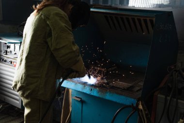 Brunette welder working with welding torch in factory  clipart