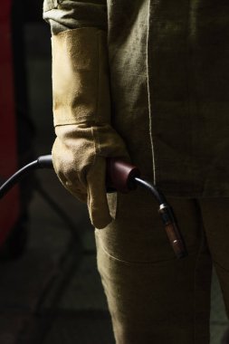 Eldivenli ve üniformalı kaynakçı fabrikada kaynak makinesi tutuyor. 