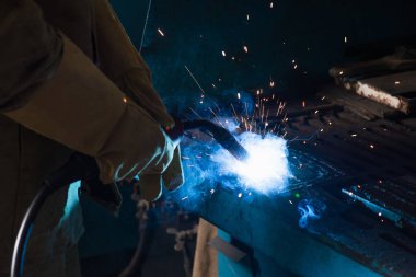 Fabrikada meşaleyle çalışan eldivenli kaynakçı görüntüsü. 