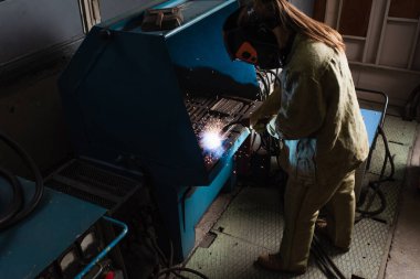 Üniformalı kaynakçının yüksek açılı görüntüsü fabrikada makinenin yanında meşaleyle çalışıyor.