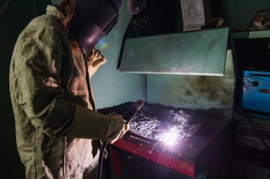 Fabrikada kaynak makinesiyle çalışan maskeli bir kaynakçı. 