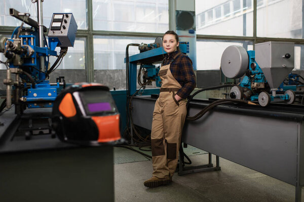 Young welder holding hand in pocket of overalls in factory 