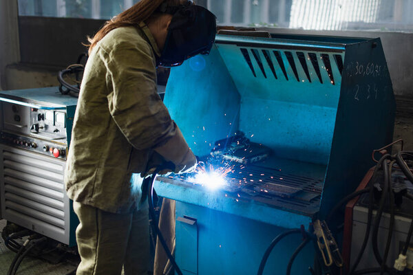Young welder working with welding torch in factory 