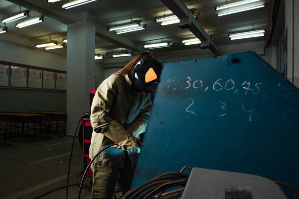 Welder in protective helmet working in factory 