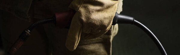 Cropped view of welder in glove holding welding torch in factory, banner 