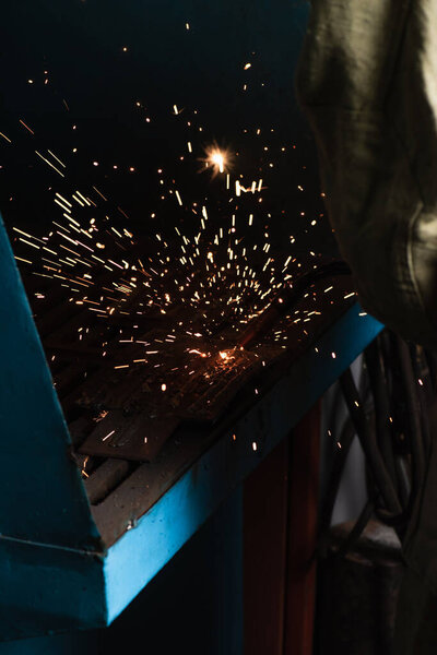 Cropped view of sparks near welder working in factory 