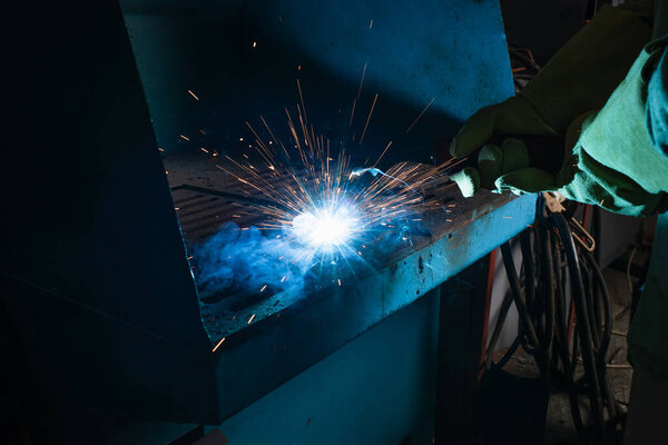 Cropped view of welder in gloves working with sparkling torch in factory 