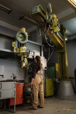 Young brunette welder tuning welding machine while working in factory  clipart