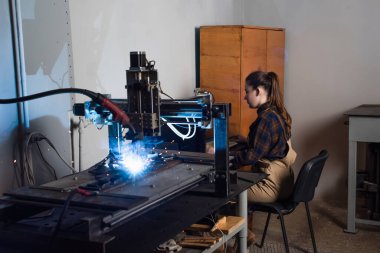 Side view of welder sitting near keyboard and welding machine in factory  clipart