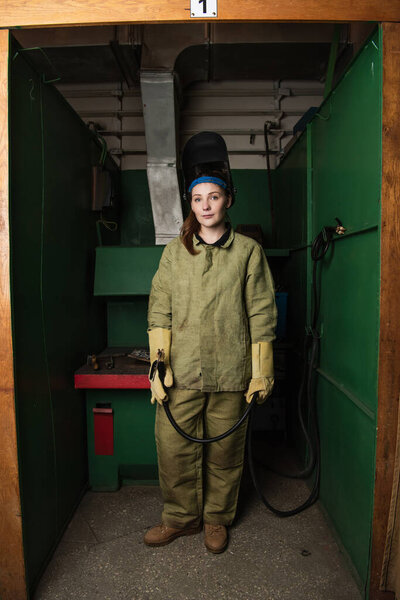 Young welder in uniform holding welding torch in factory 